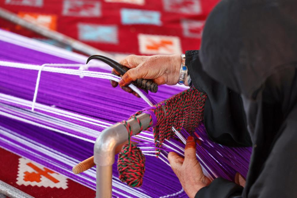 أيدٍ تعمل على نسيج السدو بخيوط ملونة.